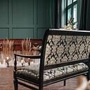 There is a room with a closed casket, surrounded by plants and with a bench sitting in front of it, as if showing a funeral service being prepared for someone who has passed away