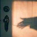 A shadowy hand reaching for an antique doorknob.