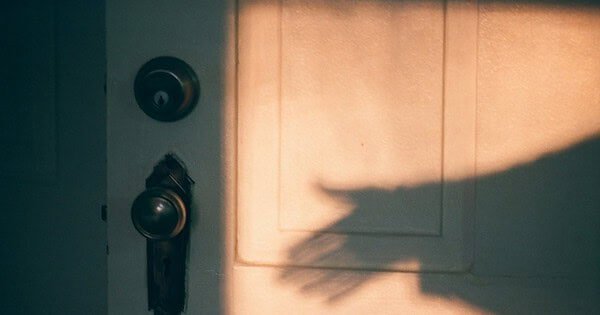 A shadowy hand reaching for an antique doorknob.