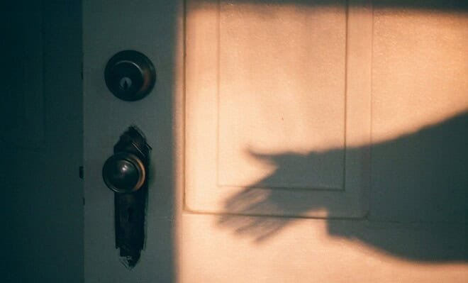 A shadowy hand reaching for an antique doorknob.