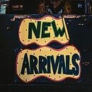 A brick background with a yellow paper with pink dots on it that reads new arrivals in dark and light green lettering