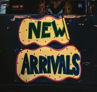 A brick background with a yellow paper with pink dots on it that reads new arrivals in dark and light green lettering