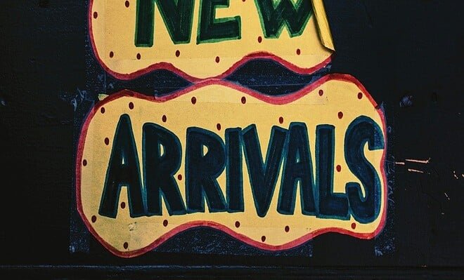 A brick background with a yellow paper with pink dots on it that reads new arrivals in dark and light green lettering