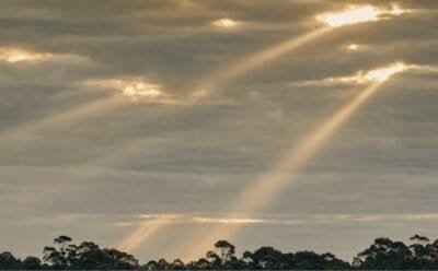 The image shows a grey twilight sky with golden sunbeams shining down from holes in the clouds
