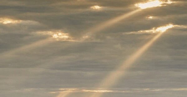 The image shows a grey twilight sky with golden sunbeams shining down from holes in the clouds