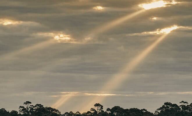 The image shows a grey twilight sky with golden sunbeams shining down from holes in the clouds
