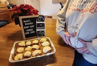 Pregnancy announcement showing a batch of cinnamon rolls with a couple holding her pregnant belly