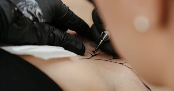 We see a tattoo artist in the middle of doing a tattoo for a client, the ink being drawn upon the clients shoulder with precision and focus