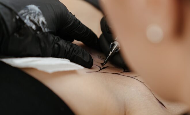 We see a tattoo artist in the middle of doing a tattoo for a client, the ink being drawn upon the clients shoulder with precision and focus