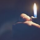 a hand reaching out of a blue, hazy background holding a lit lighter