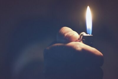 a hand reaching out of a blue, hazy background holding a lit lighter