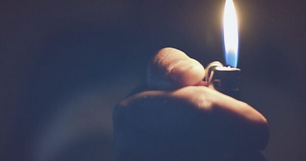 a hand reaching out of a blue, hazy background holding a lit lighter