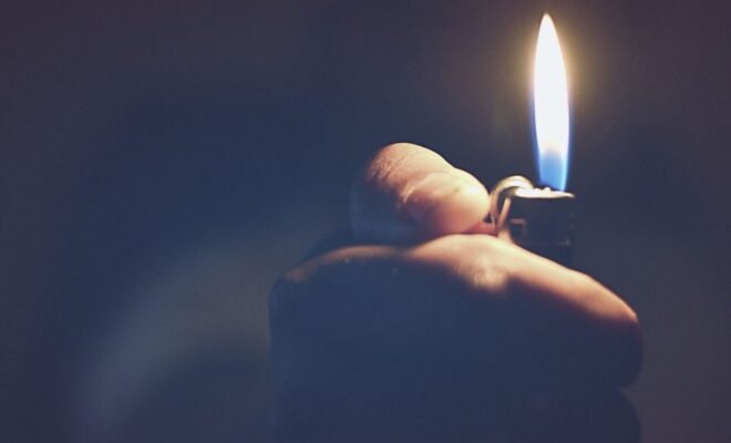 a hand reaching out of a blue, hazy background holding a lit lighter